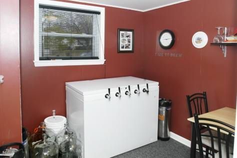 A white chest freezer with beer taps in a room with burgundy walls; a dining table and homebrew equipment present.