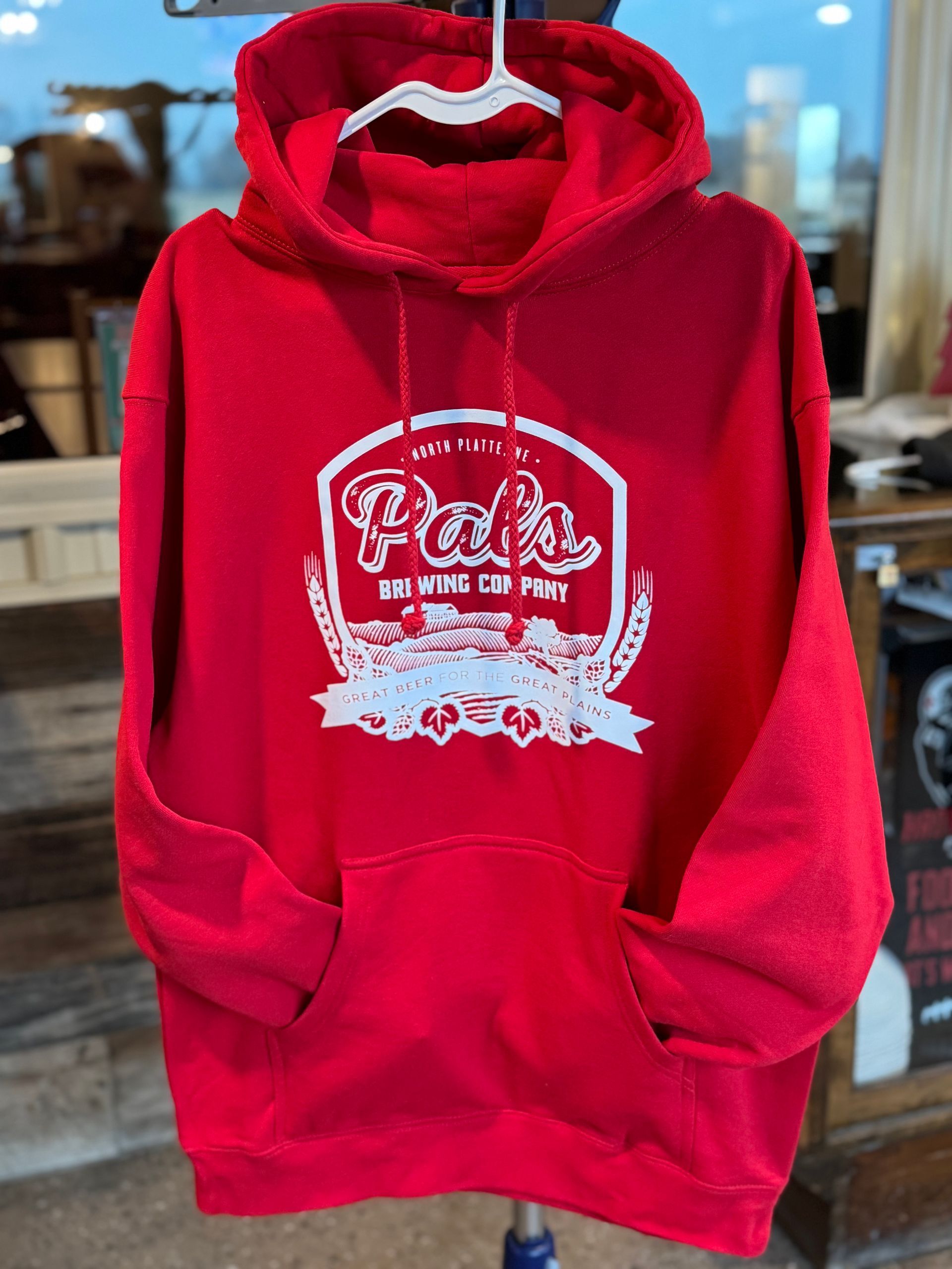 Red hoodie with a white logo, hanging on a white hanger. The logo includes the word 