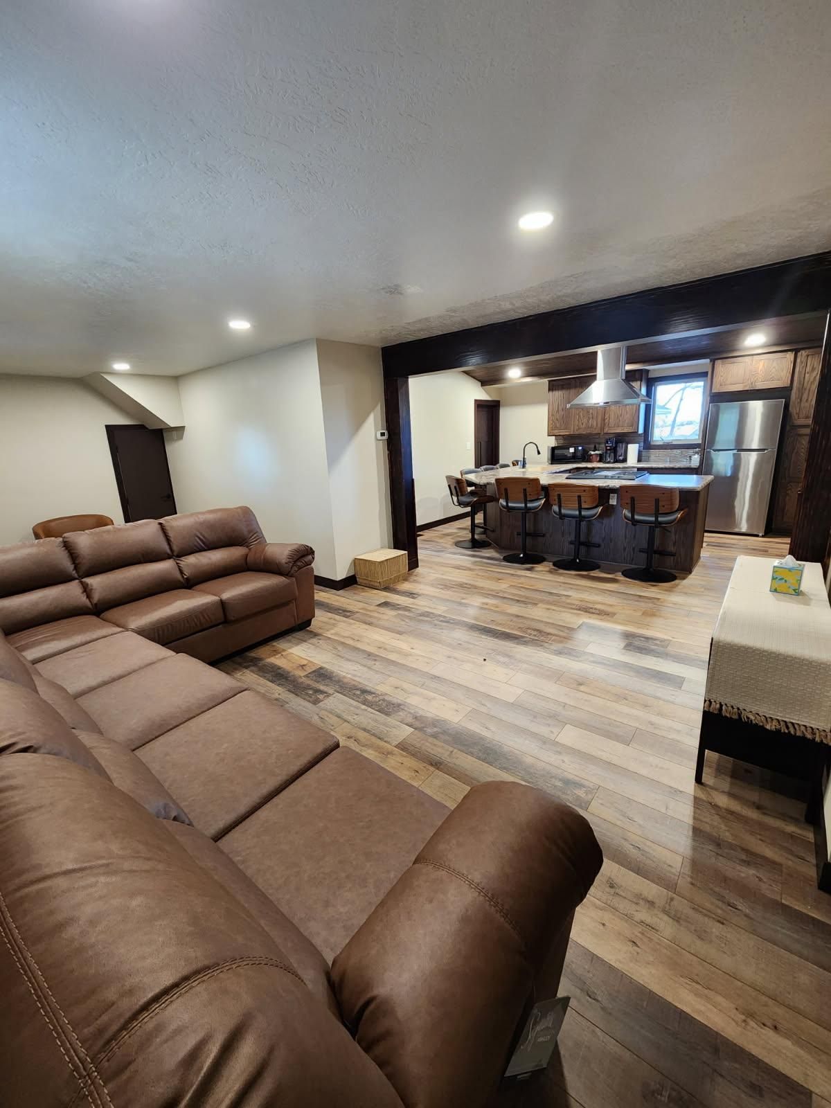 Spacious, open-concept living space with leather sofa, wood floors, and kitchen with island.