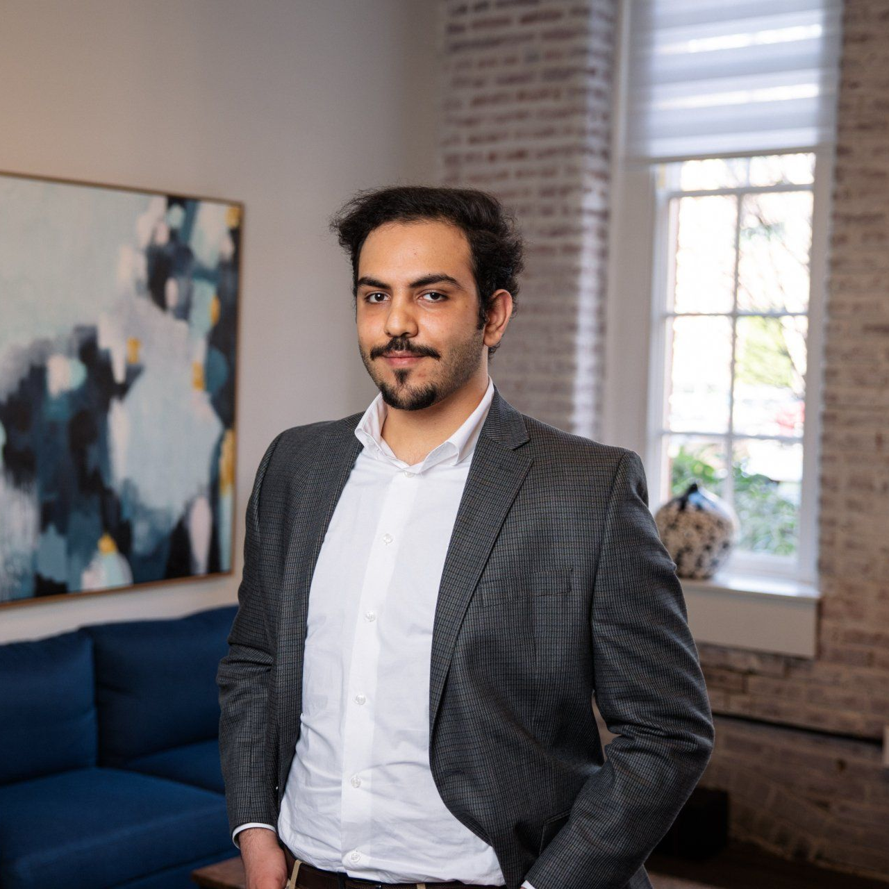 Man in a gray blazer standing in a bright living room with a blue couch and abstract wall art