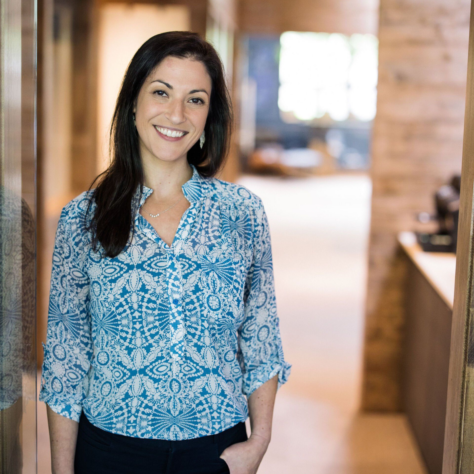 Smiling woman in a blue patterned blouse standing in a bright hallway