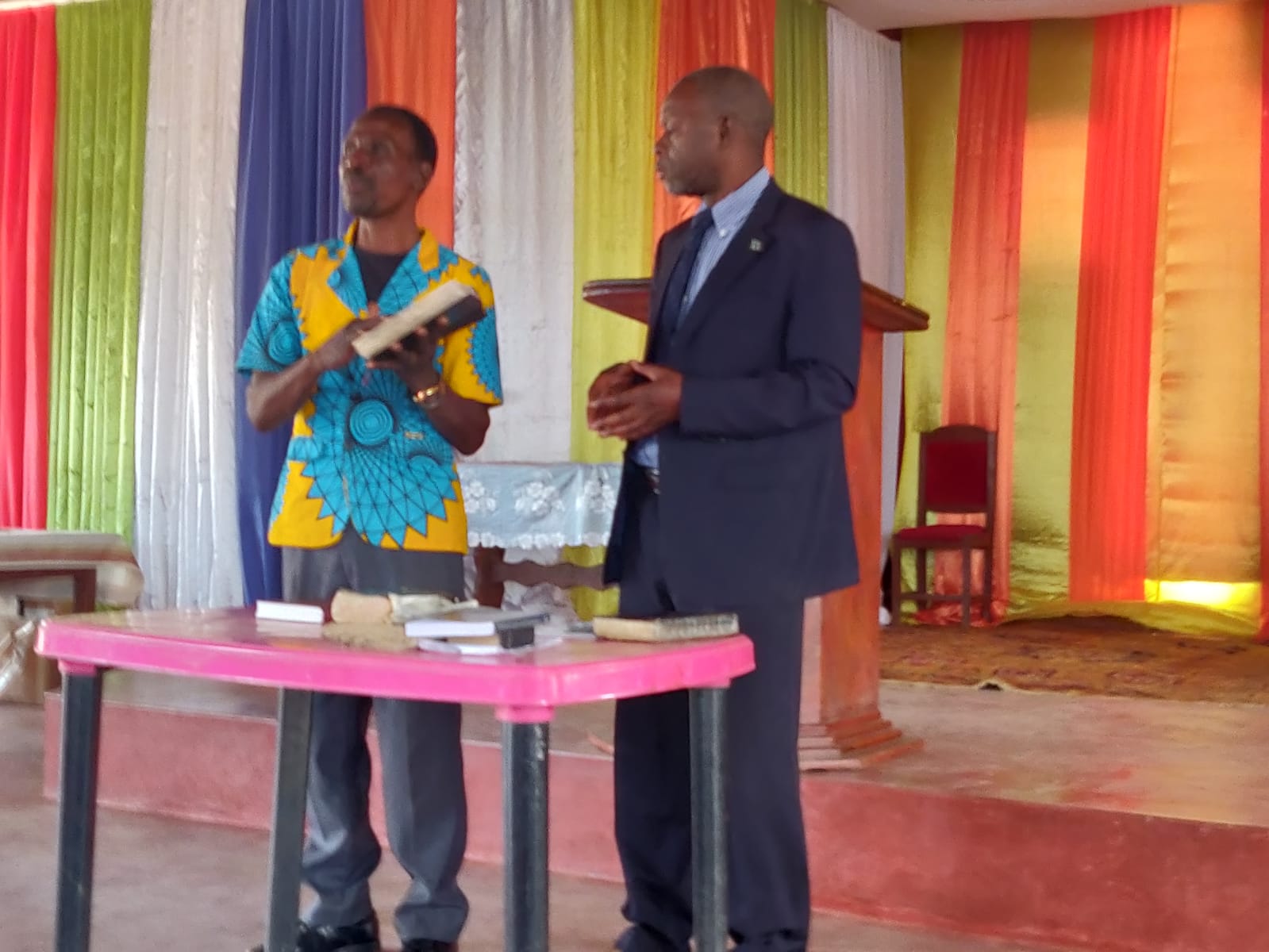 A man in a suit stands next to another man holding a book