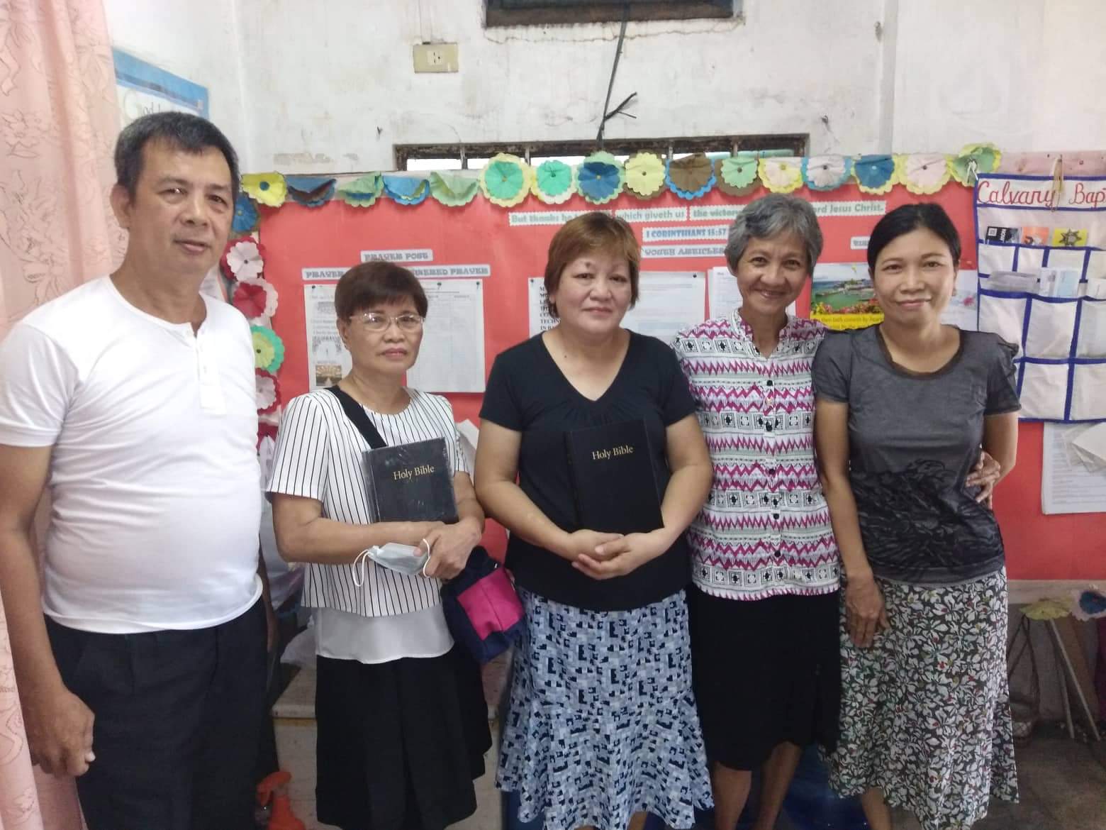 A group of people posing for a picture in front of a bulletin board