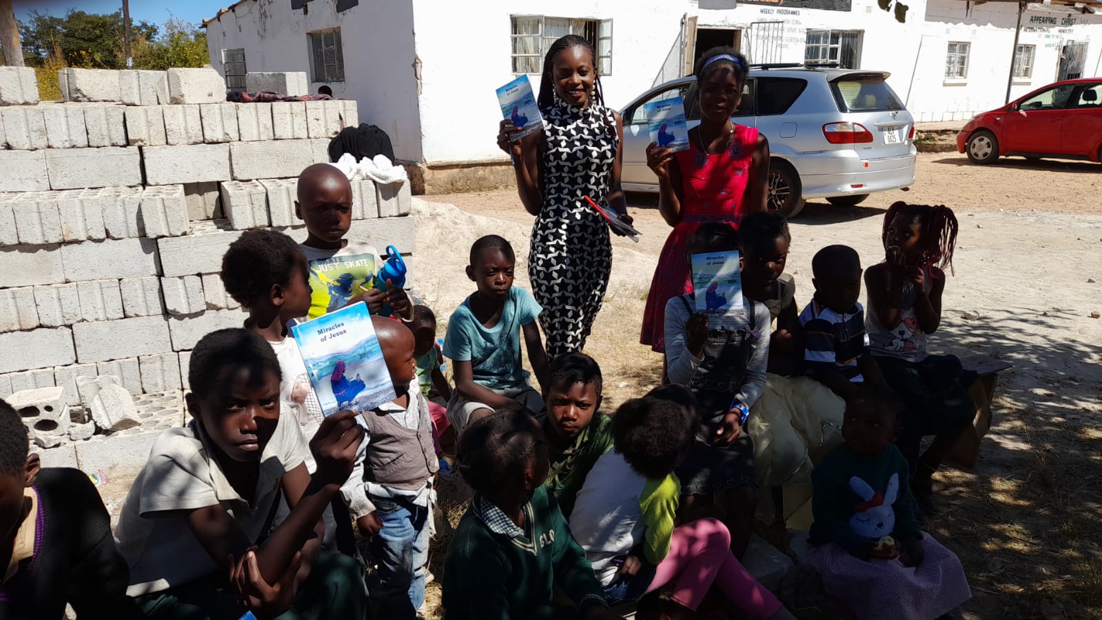 A group of children are sitting on the ground in a parking lot.
