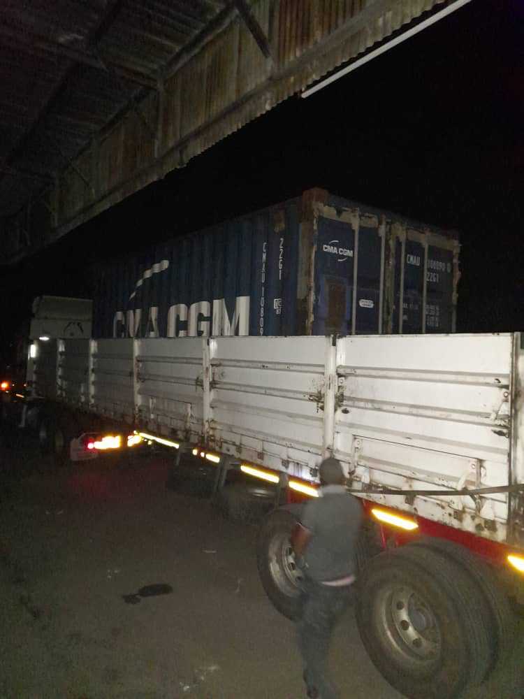 A man is standing next to a semi truck with a container on the back.