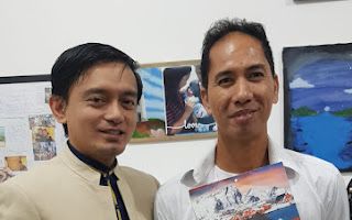 Two men are posing for a picture and one of them is holding a book.