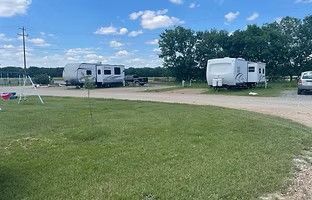Two travel trailers parked in a grassy, open lot under a bright blue, partly cloudy sky.