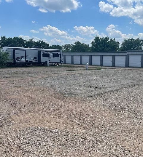 A large RV parked on a gravel lot next to a row of white storage units under a blue, cloudy sky.