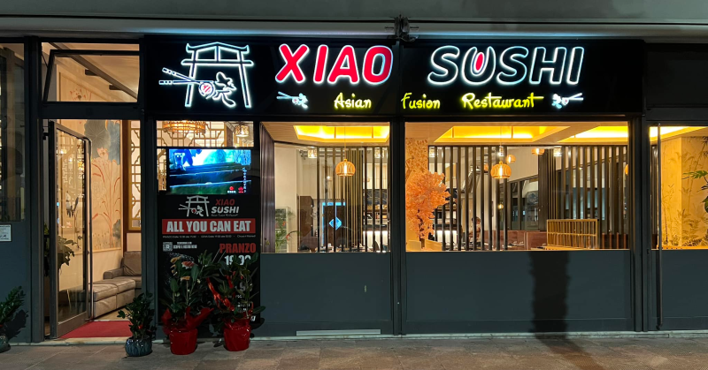 La facciata notturna del ristorante Xiao Sushi, con insegna al neon e vetrine illuminate.