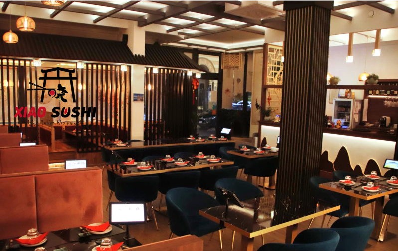 Elegante interno di un ristorante di sushi con decorazioni in legno, tavoli apparecchiati per la cena e calda illuminazione d'ambiente.