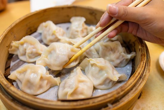 Ravioli al vapore in un cestino di bambù, con le bacchette che si allungano per prenderne uno