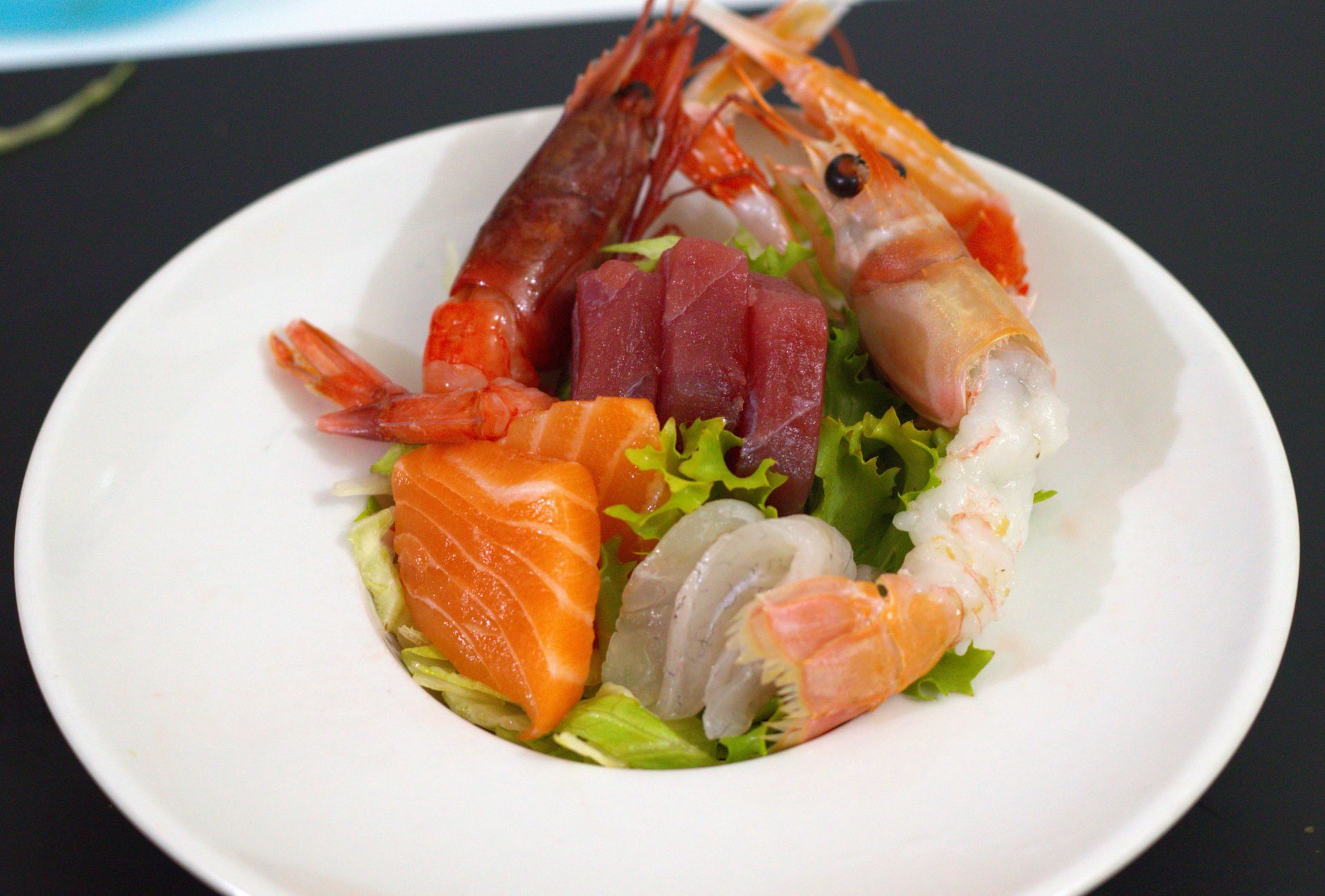 Sashimi misto su un piatto bianco con salmone, tonno, gamberi e verdure.
