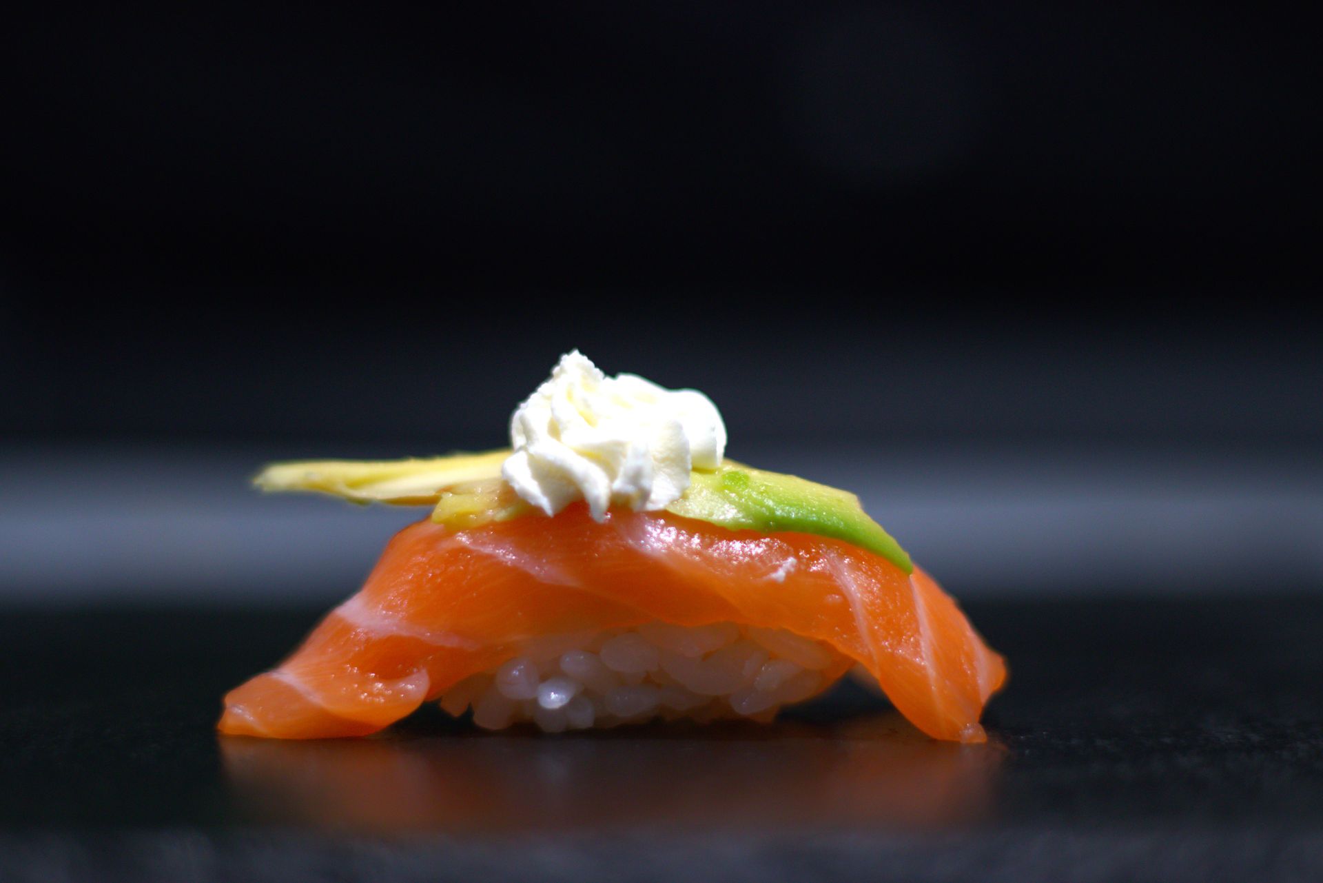 Nigiri di sushi al salmone con wasabi e una cucchiaiata di panna su una superficie scura