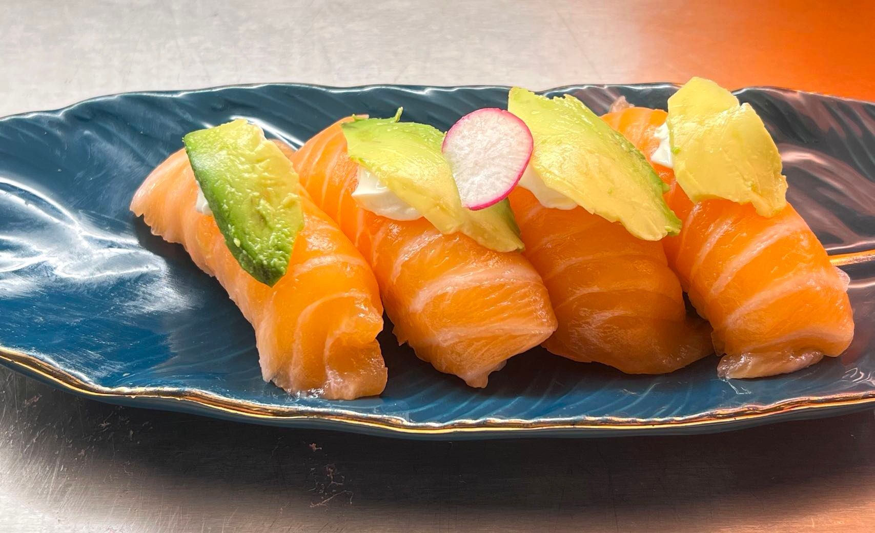 Nigiri di salmone su un piatto di ceramica scura, guarnito con fette di agrumi.