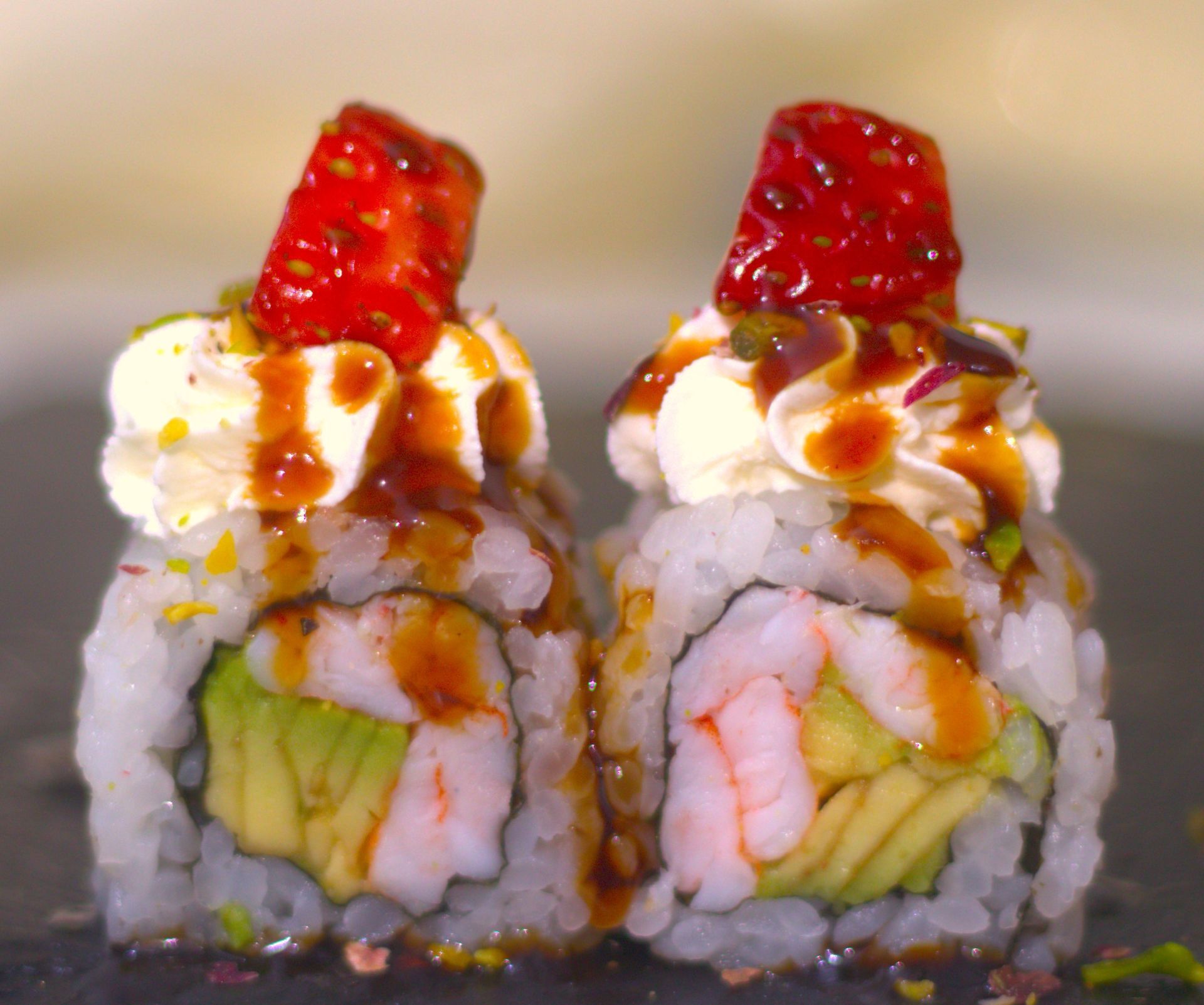 Due involtini di sushi guarniti con avocado, gamberi, salsa cremosa e caviale rosso, su un piatto scuro.