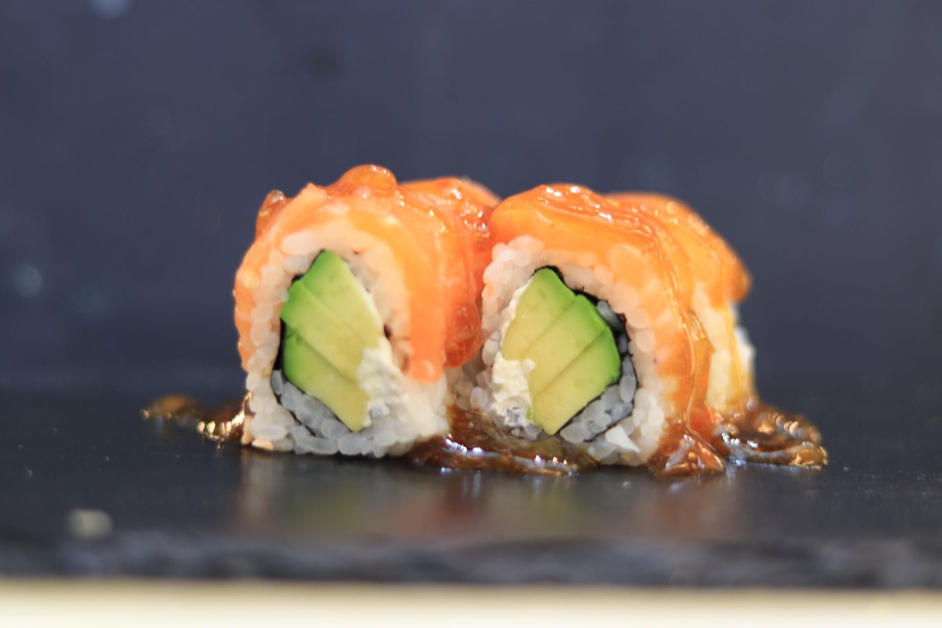 Due pezzi di sushi di salmone e avocado su un piatto scuro