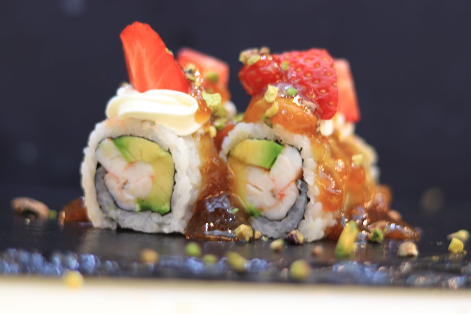 Rotoli di sushi guarniti con fragole e salsa su un piatto scuro