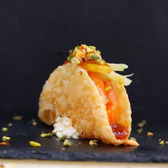 Taco con guscio croccante, pomodoro, formaggio e guarnizione su sfondo scuro