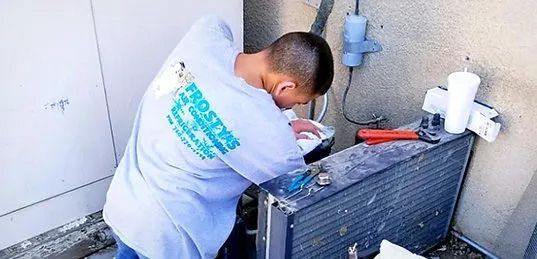 A man is working on an air conditioner outside of a building.