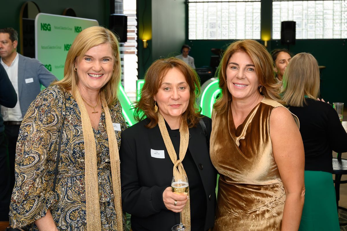 Three people smiling together at a professional event with green branding in the background.