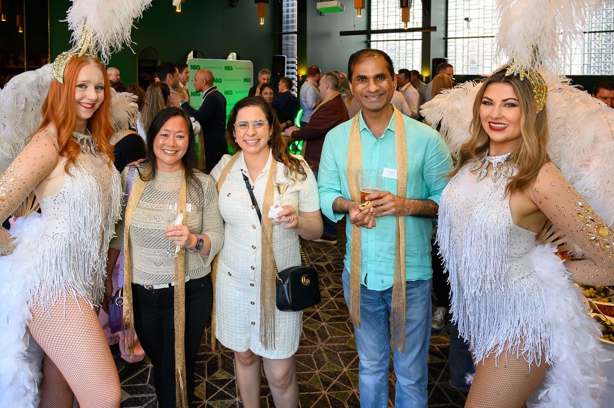 Four people posing at an event, including two entertainers in white feathered costumes and two people in casual attire.