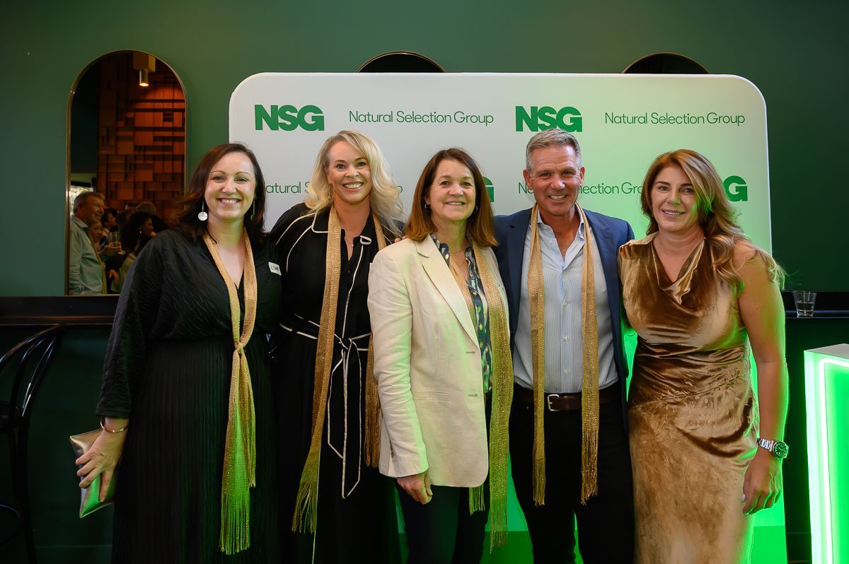 Five people pose smiling in front of an NSG banner at an indoor event, wearing scarves and formal attire.