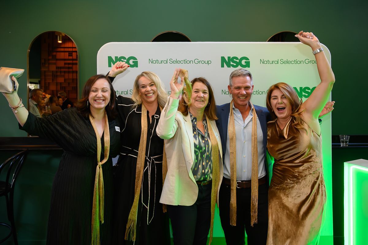 Five people posing happily in front of a green and white 