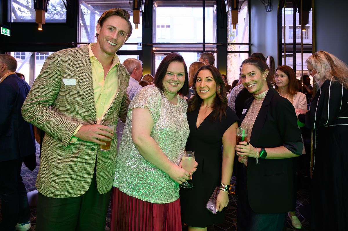 A group of four people smiling and posing for a photo at an indoor social event with dark, modern decor.