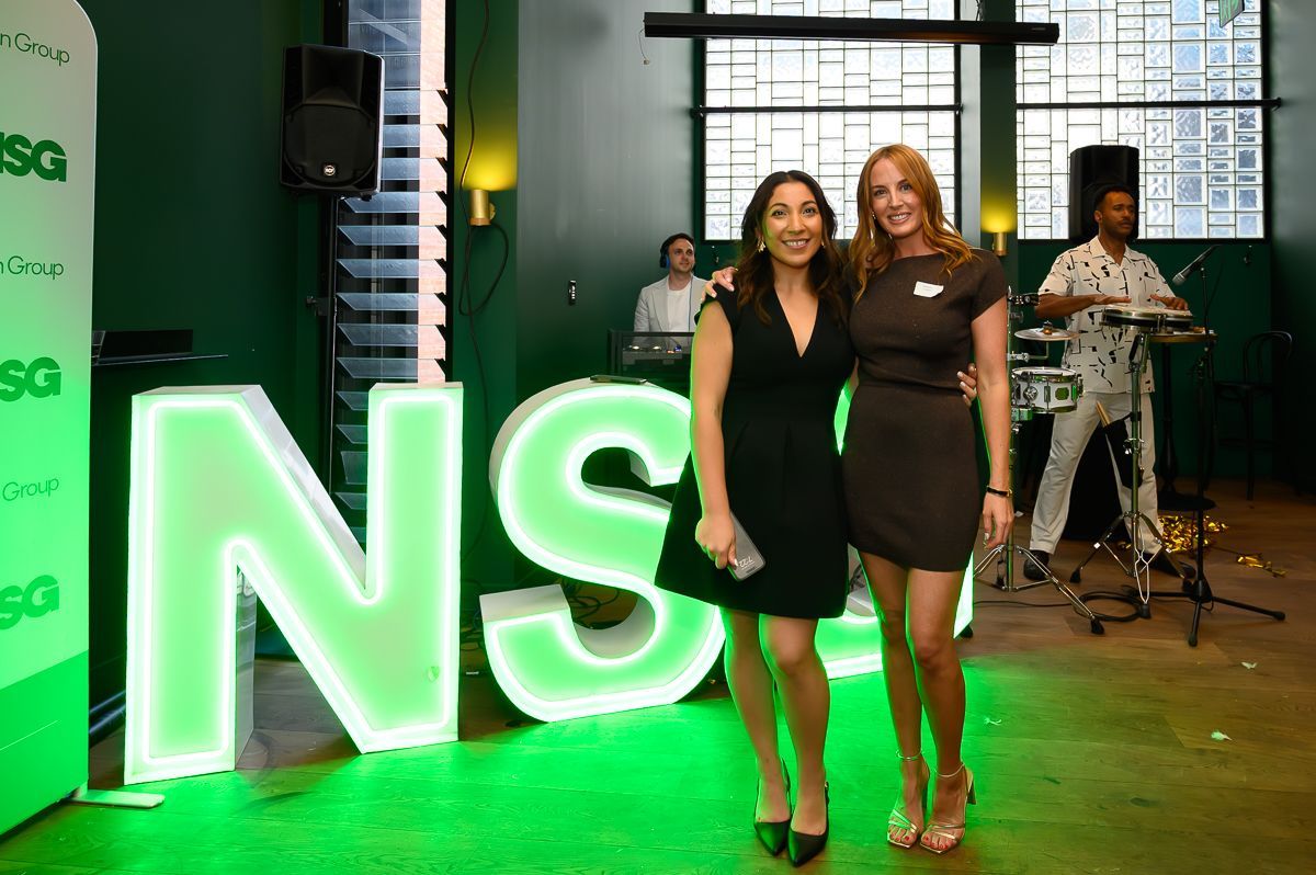 Two people stand smiling in front of large, glowing green 