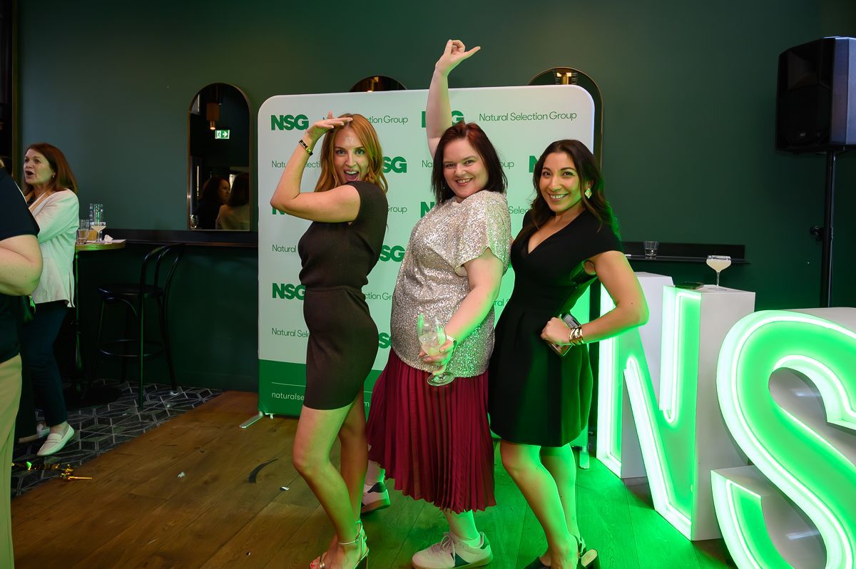 Three people pose playfully in front of a green 