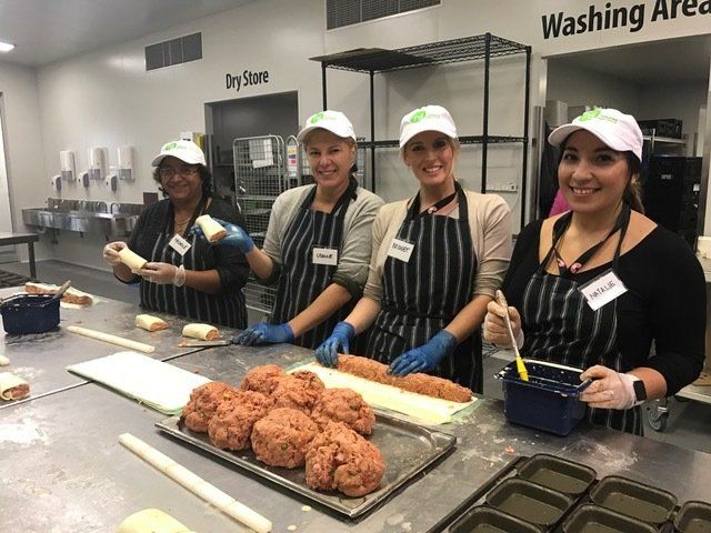 Four people in white hats and black aprons prepare food in a commercial kitchen.