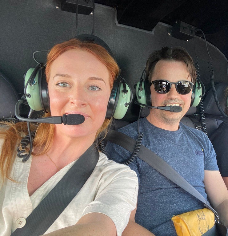A woman and a man wearing aviation headsets inside a helicopter.