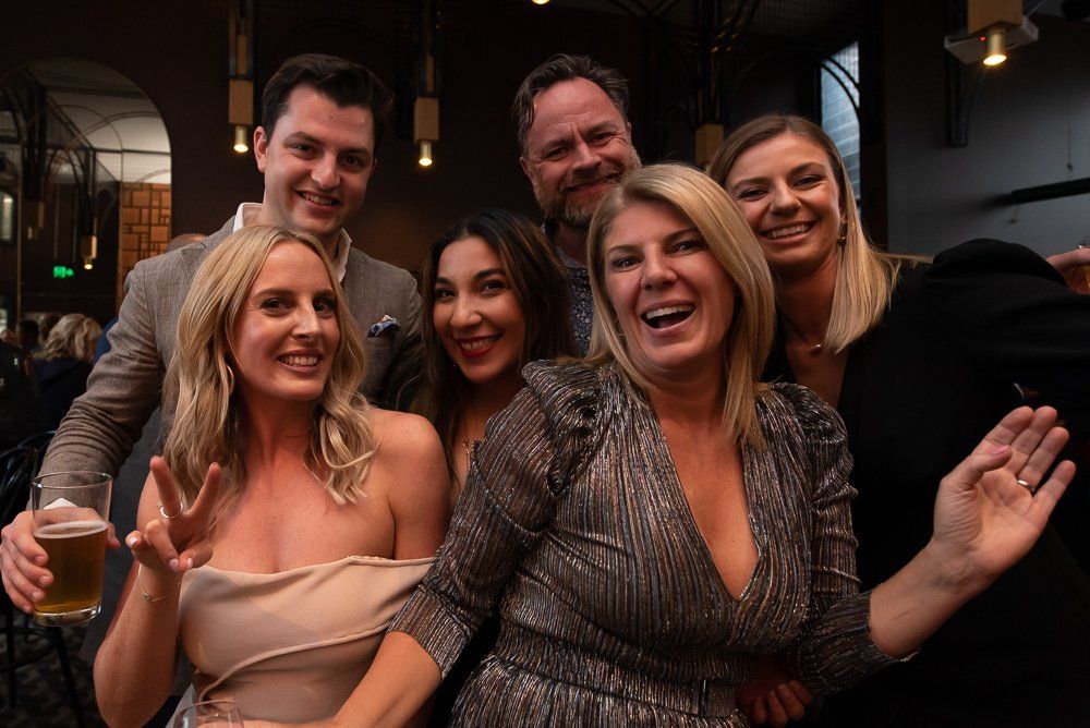 A group of six people posing together for a celebratory photo at an indoor evening venue.
