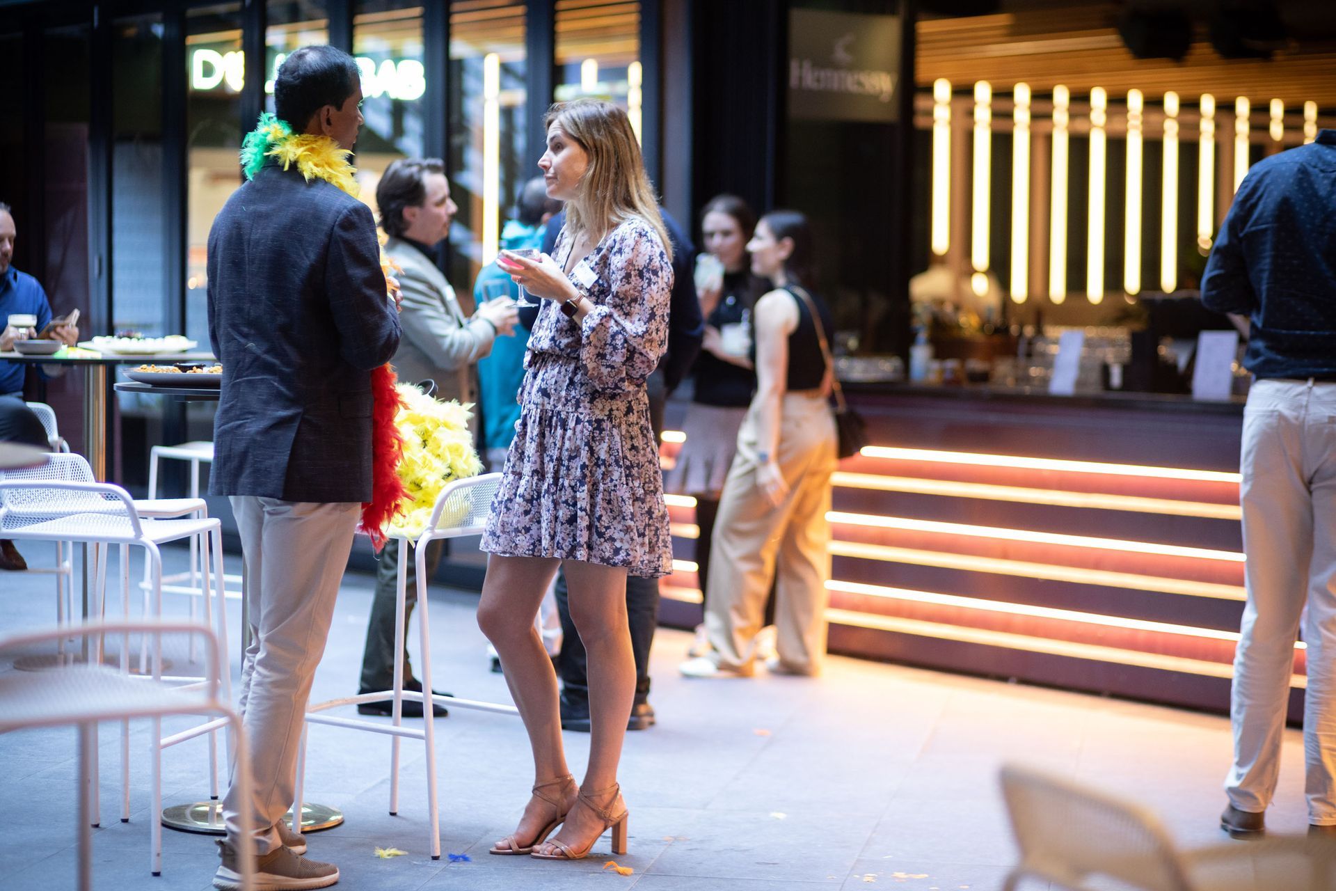 A group of people socializing at an indoor bar event with warm lighting and a modern, social atmosphere.