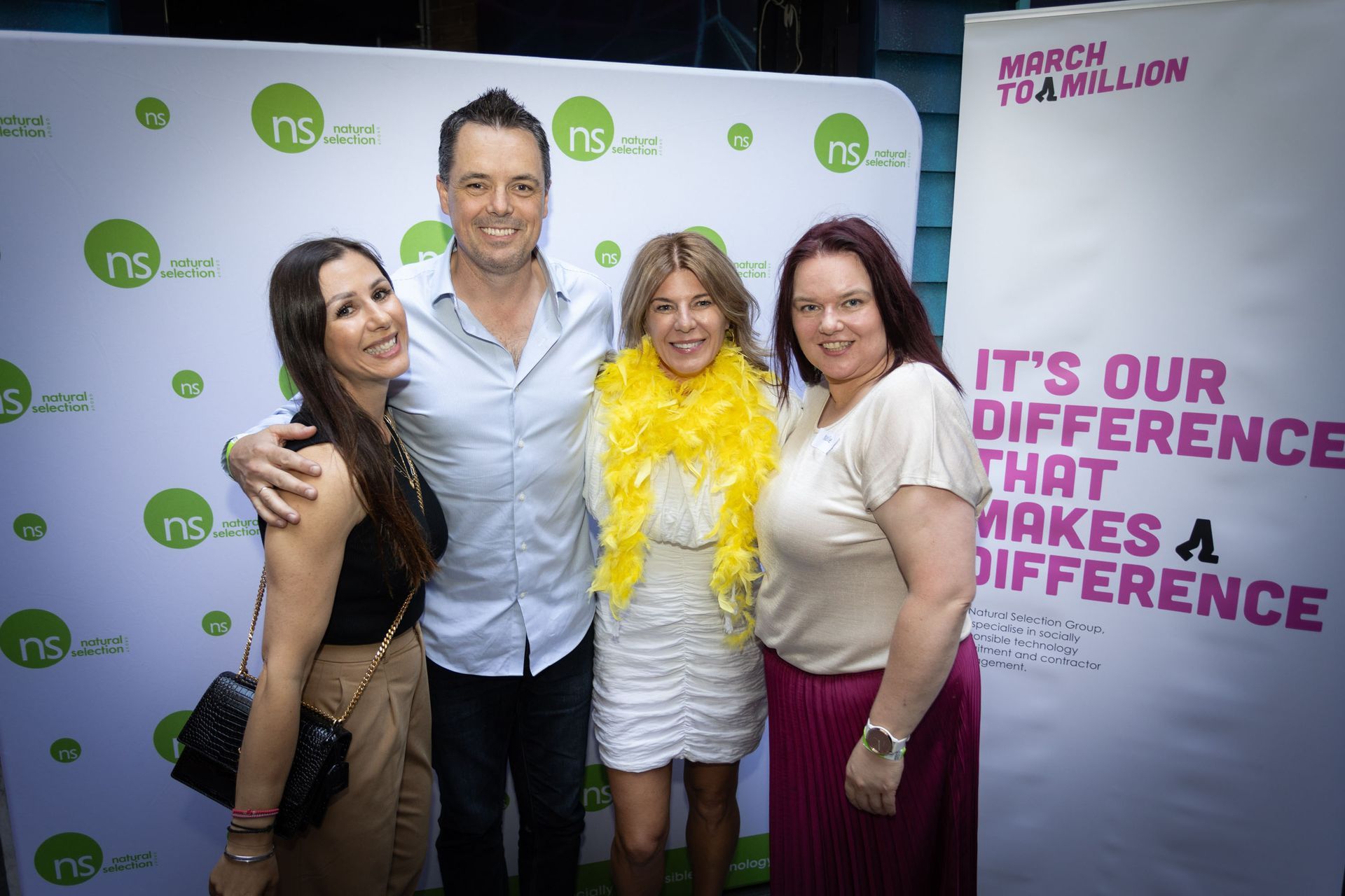 Four people pose for a photo in front of a white branded banner featuring the text 