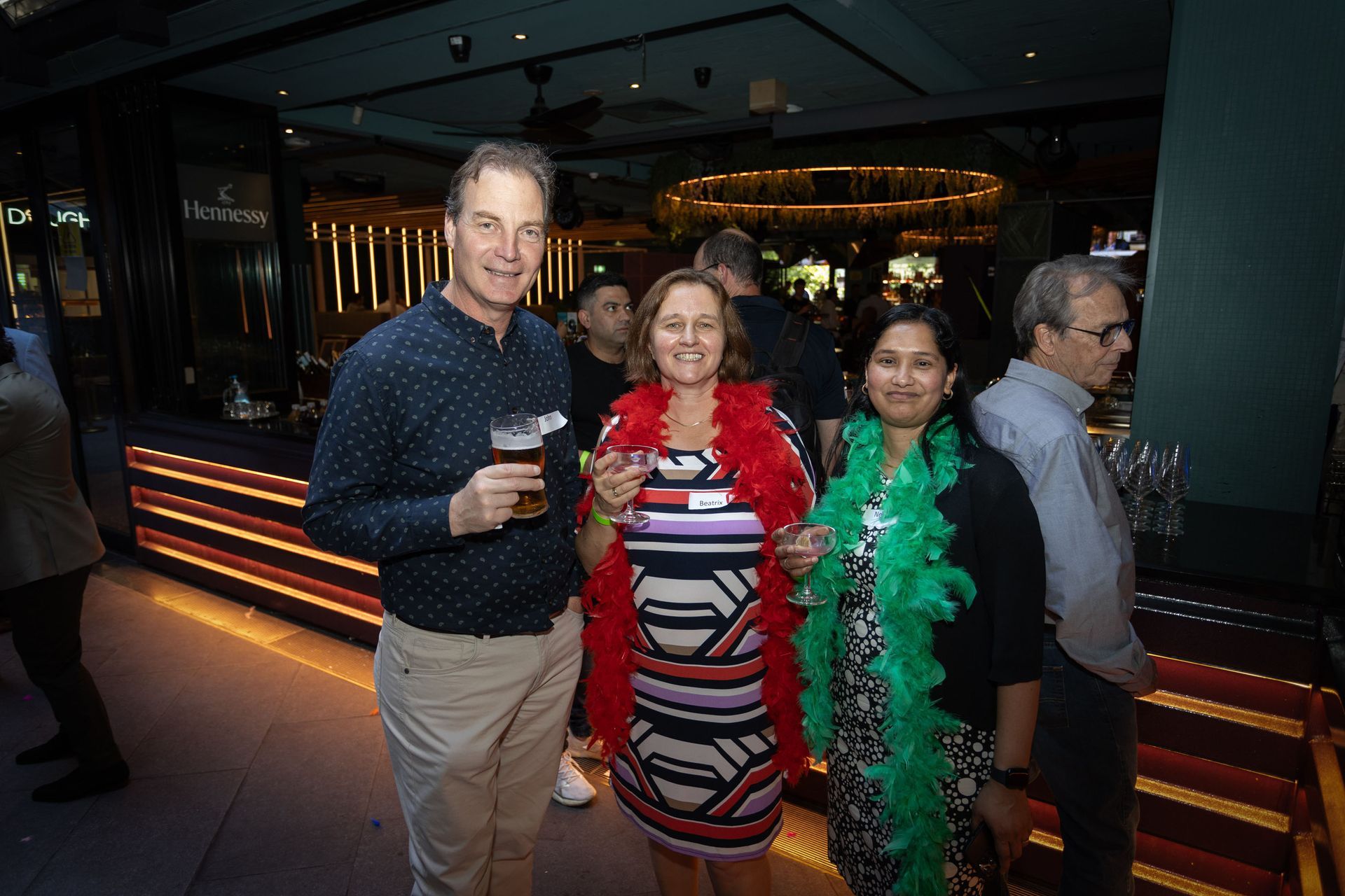 Four people standing at an evening event, with two women wearing red and green feather boas.