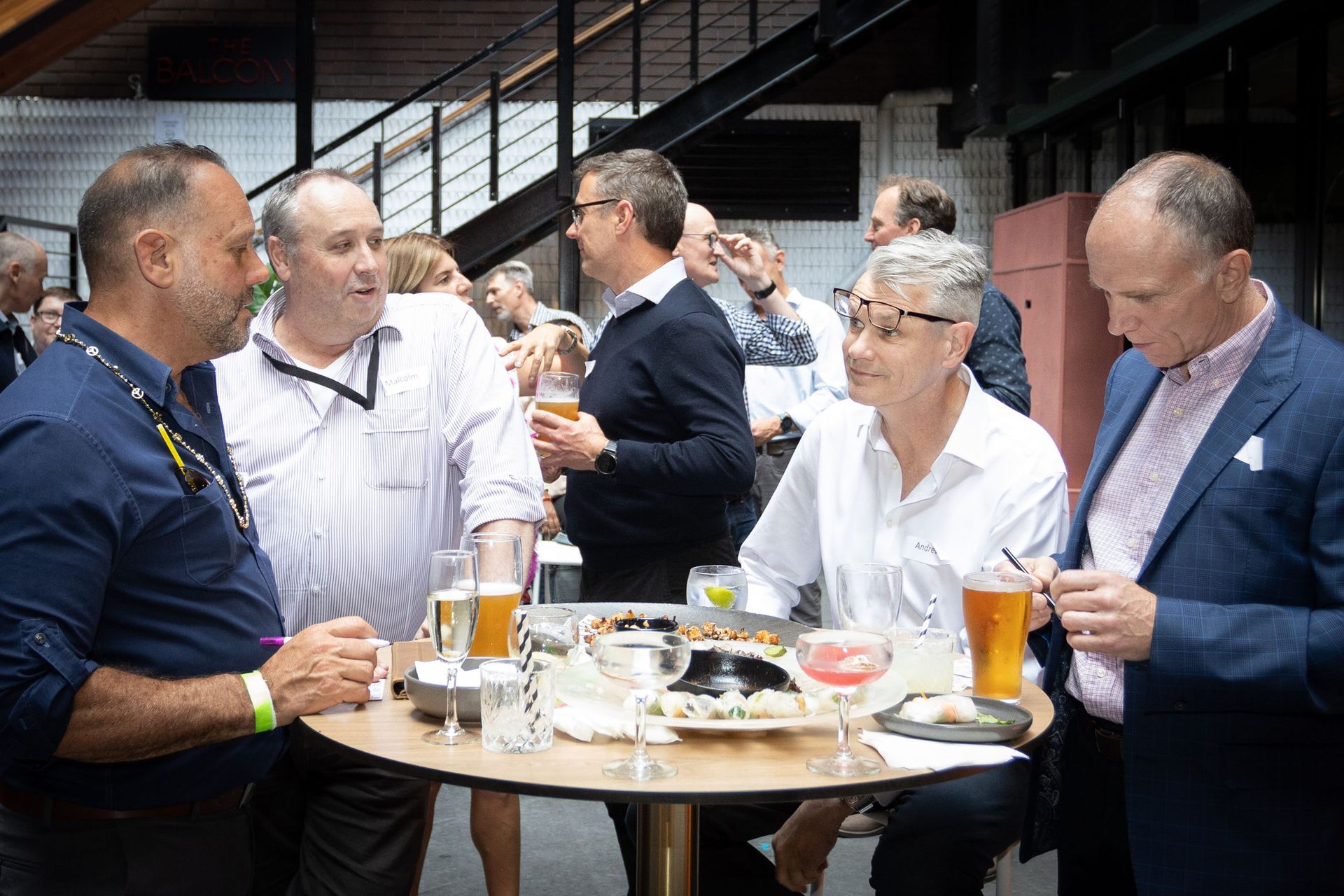 A group of people standing around a high table with drinks and food in a social or networking setting.