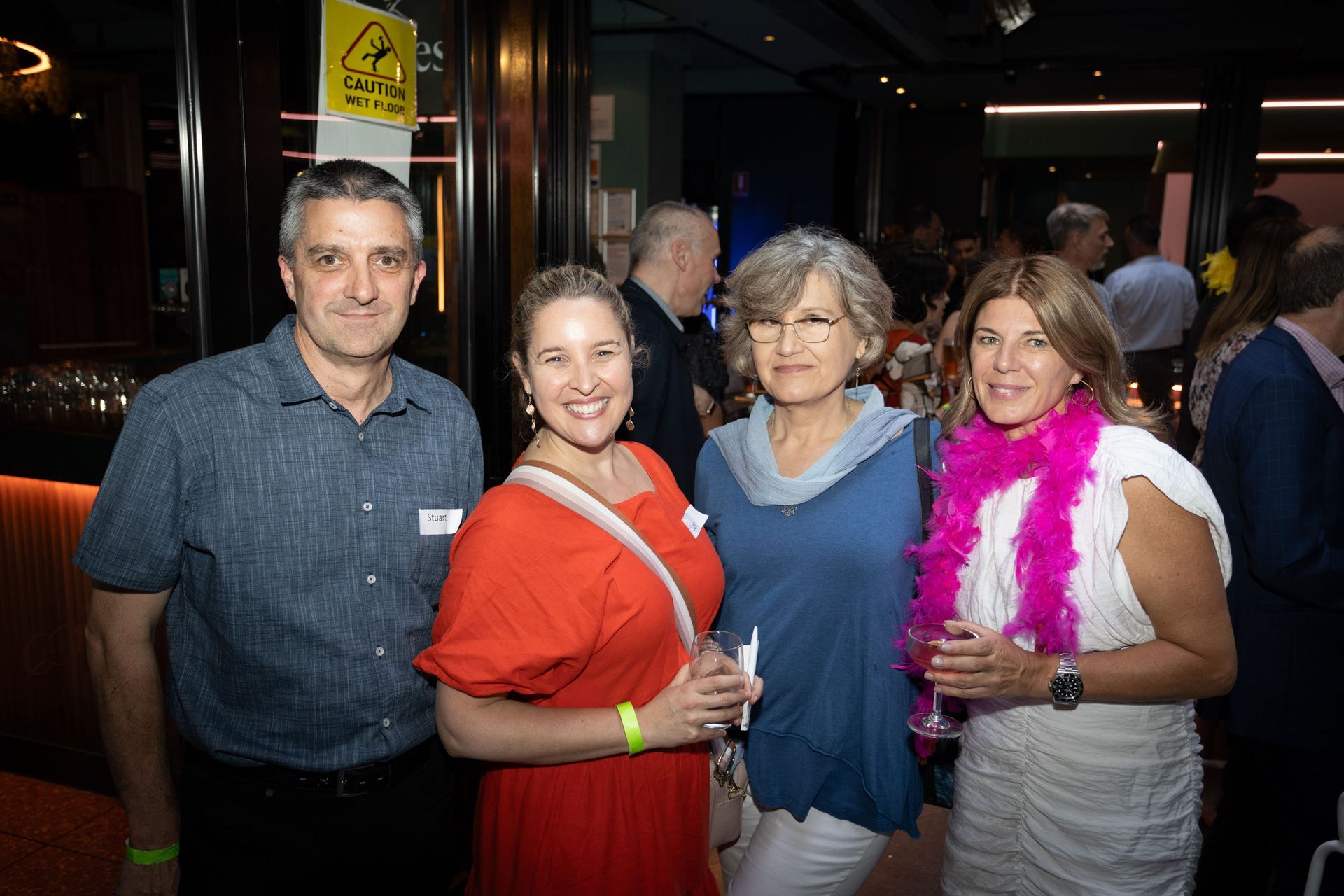 Four people stand together indoors at a social gathering, smiling as they face the camera.