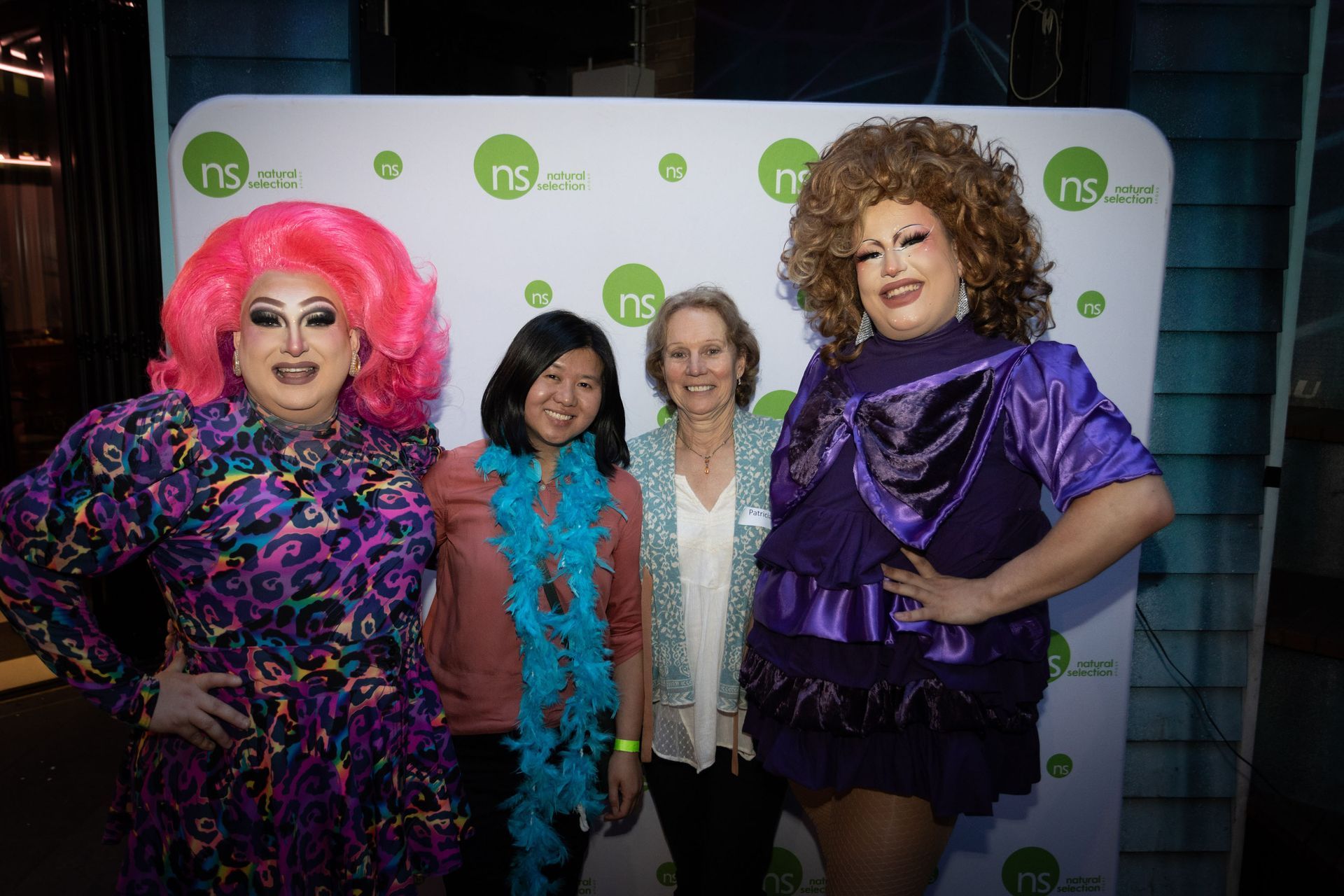 Four people stand side-by-side in front of a white backdrop with green logos, smiling for a photo.
