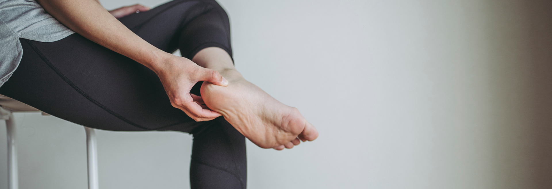 Person sitting on a chair, rubbing their ankle in black leggings and sandals