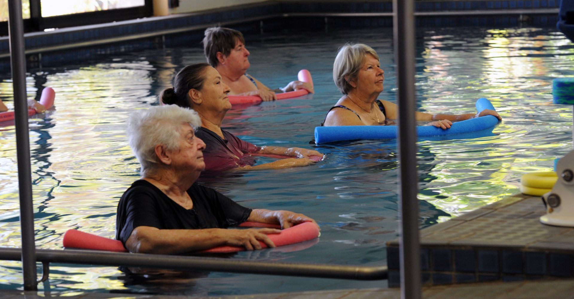 People exercising in an indoor pool using colorful foam noodles during aqua exercise class