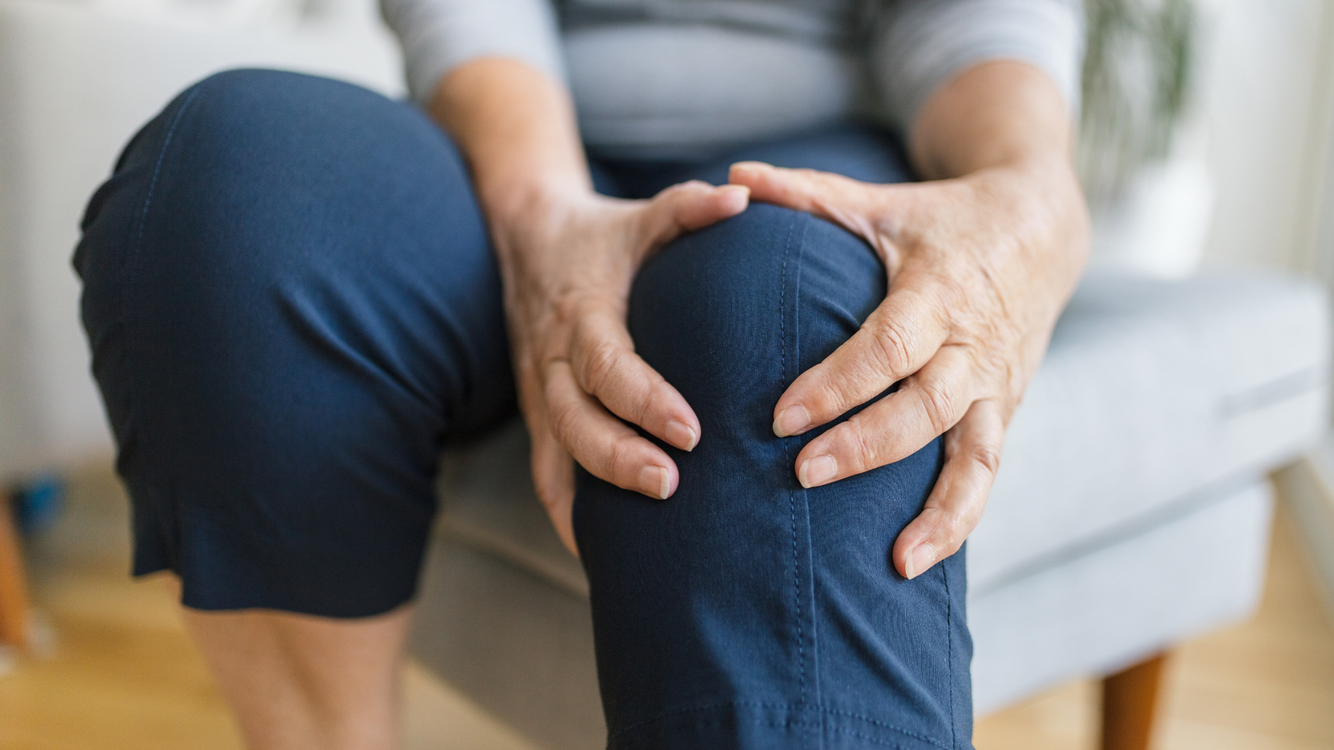 Person holding a bent knee in pain while sitting on a couch