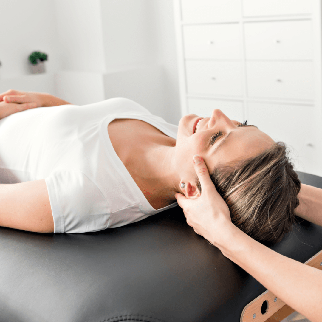 Person massaging the back of their neck in a gray shirt, with a hand reaching over the shoulder