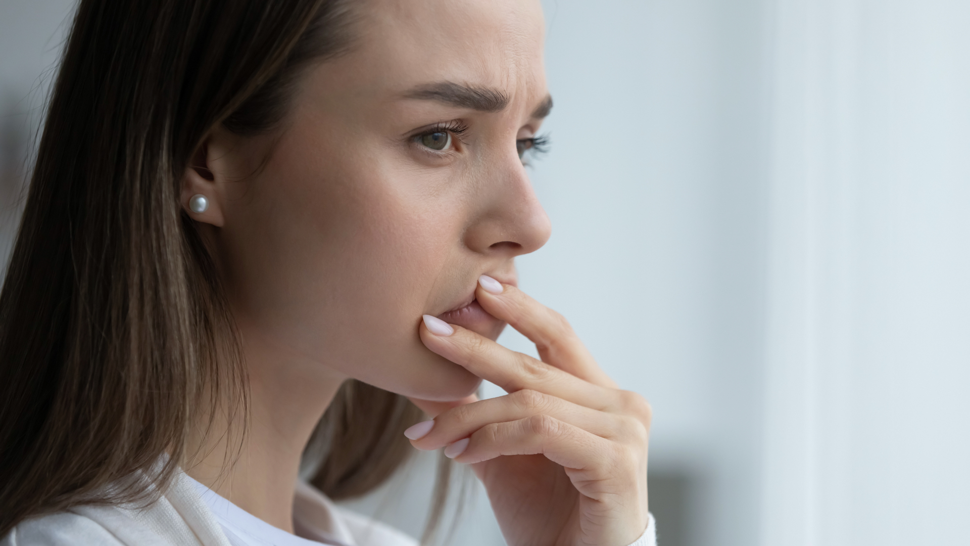 Woman in profile with fingers near her lips, staring pensively out a window