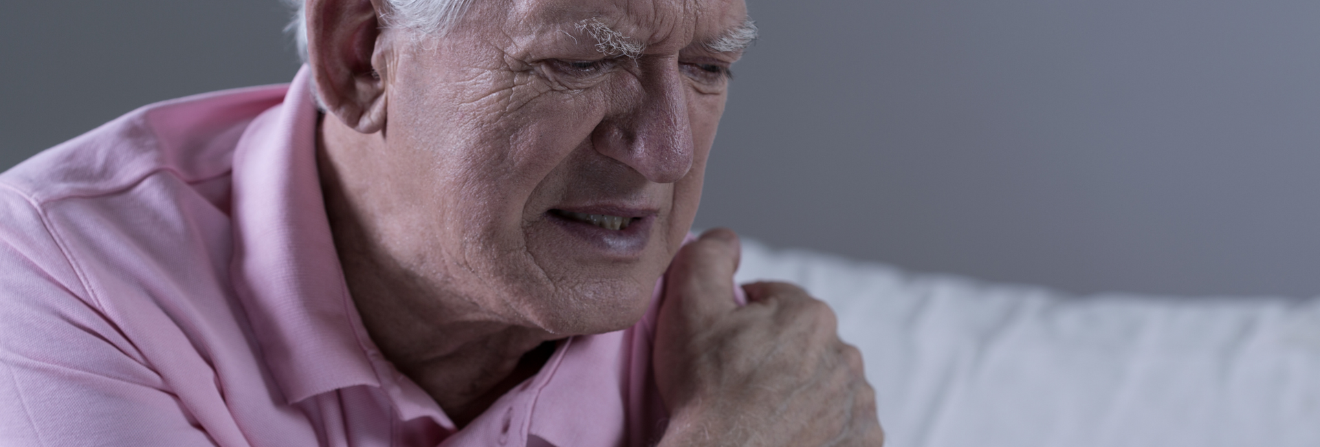 Person in a pink shirt clutching their shoulder, grimacing in pain on a couch.