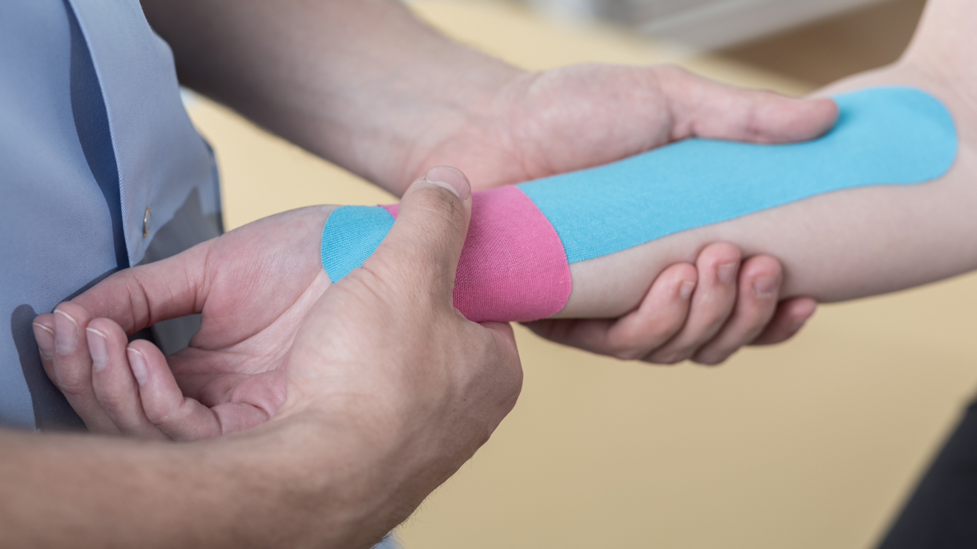 Hands holding a forearm wrapped with blue and pink athletic tape during treatment