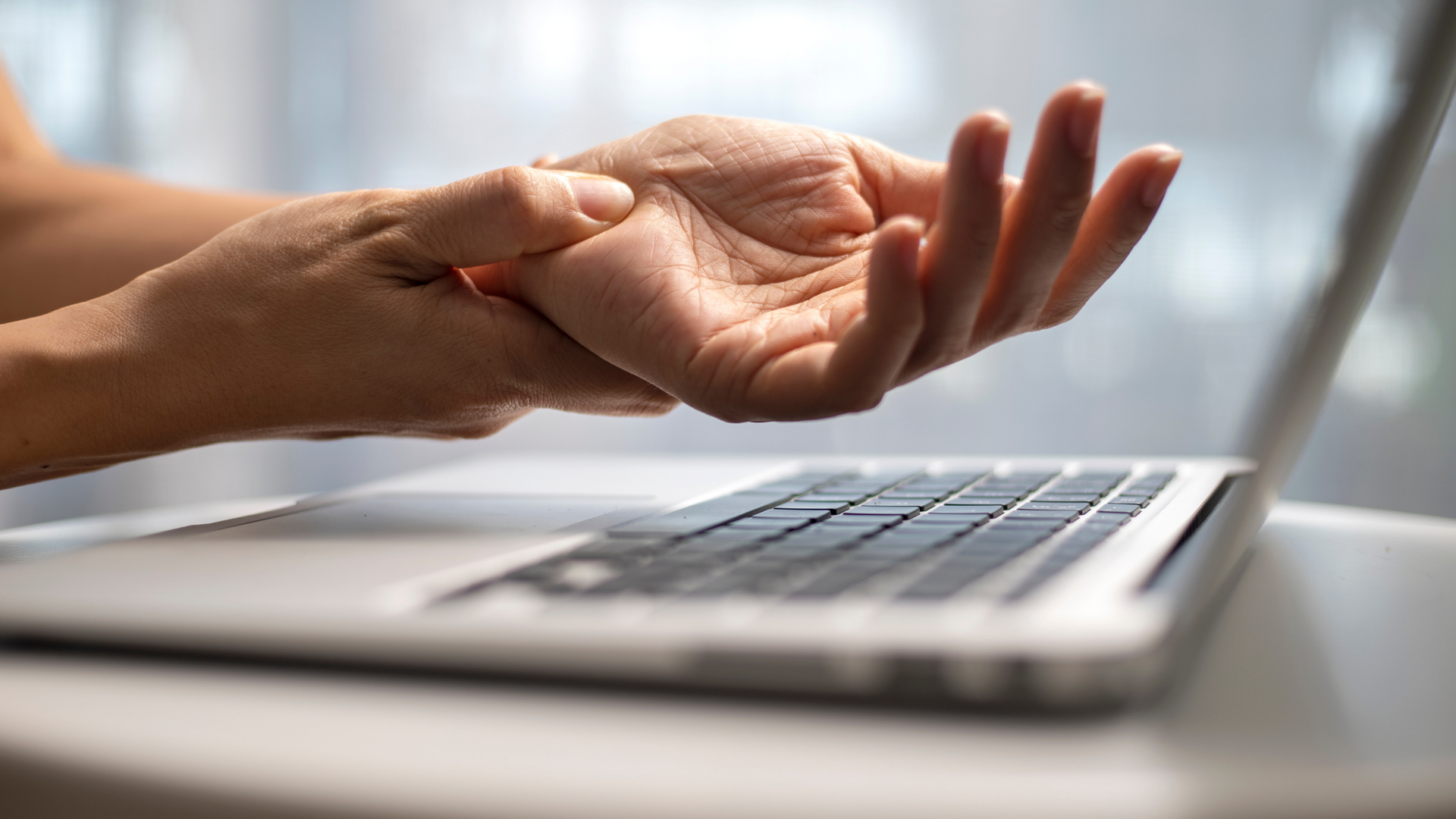 Hand reaching out above a laptop keyboard on a desk