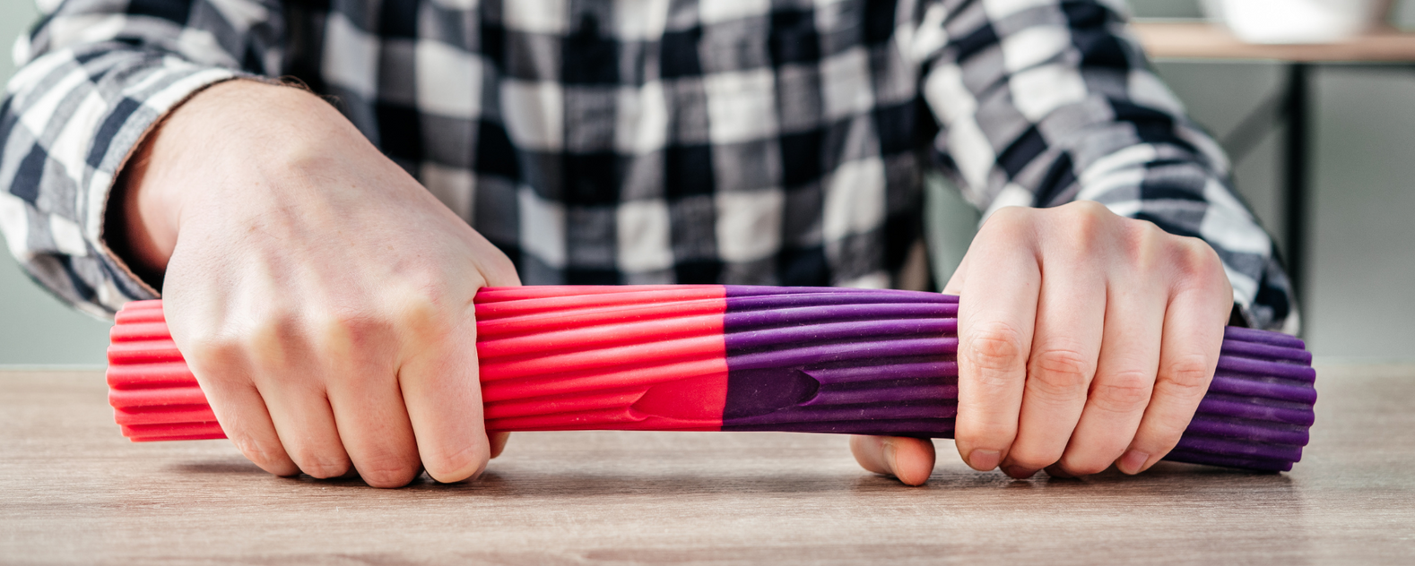 Hands stretching a red and purple resistance band on a tabletop