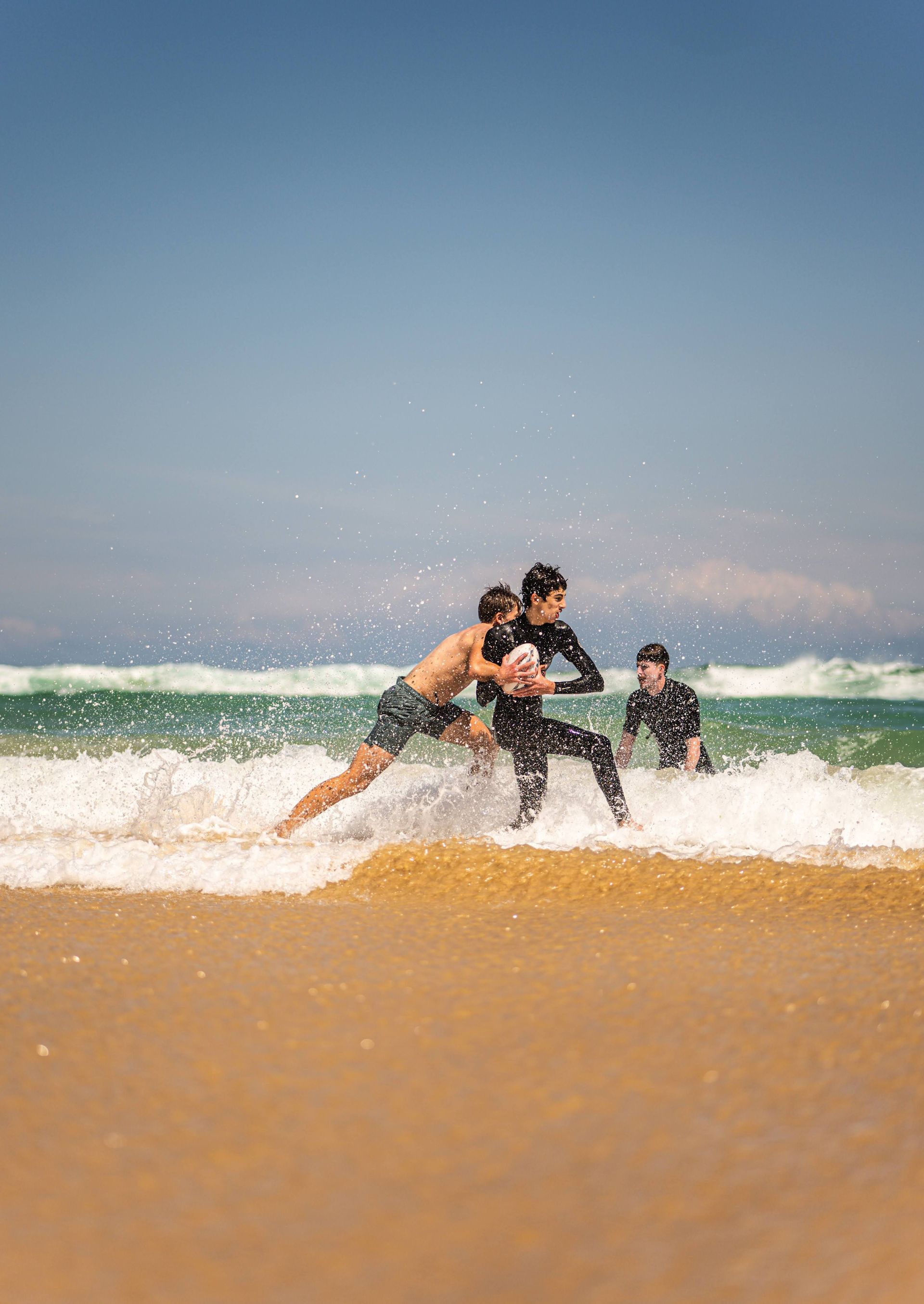 Two people wrestling in the surf on a sandy beach under a clear blue sky