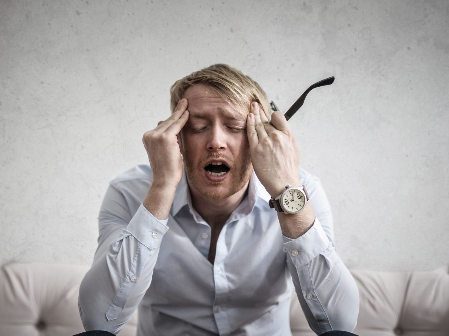 Stressed person in a white shirt holding their head on a couch, with a black umbrella behind them